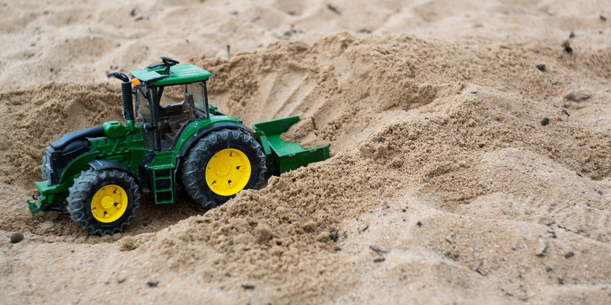 Green and black tractor in sand