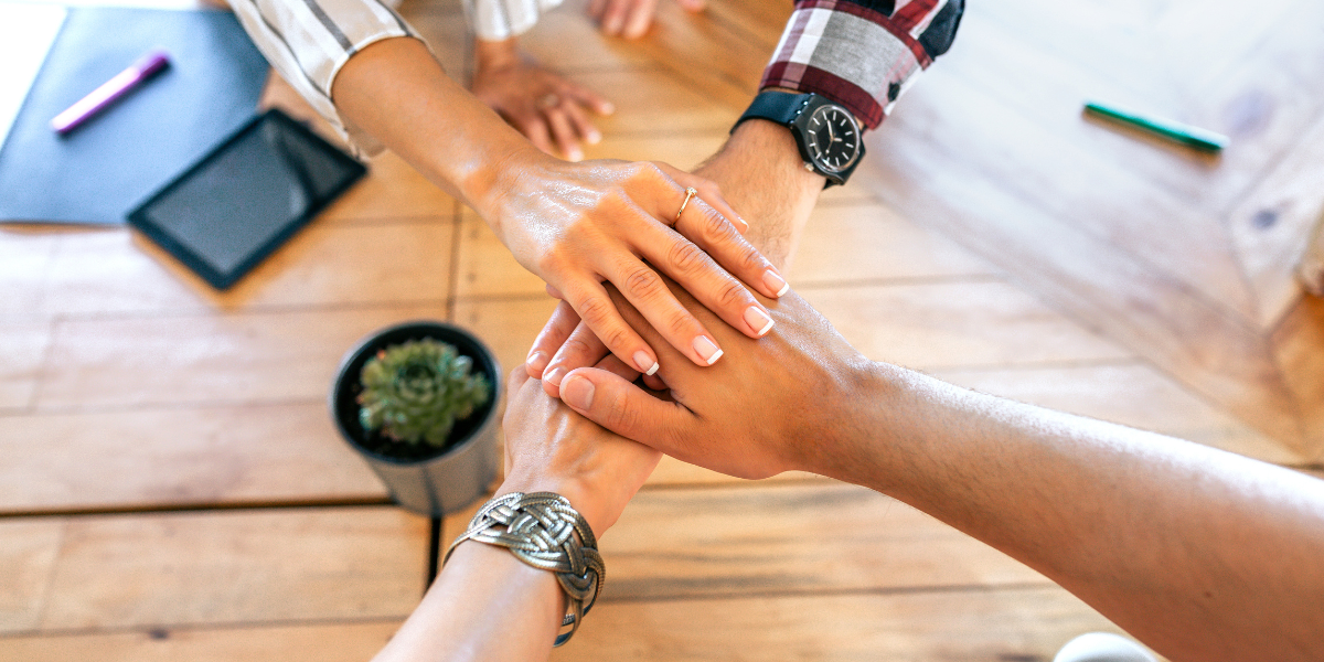Grant managers putting their hands together in the office for reducing grant program staff turnover